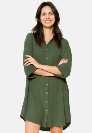 Short green button-up dress with short sleeves, featuring a slightly curved hem and a smooth texture. Gold buttons add a subtle accent.