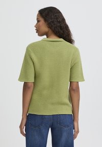 Polo vert en maille à manches courtes, avec un motif texturé et un col. Associé à un jean bleu, affichant une coupe décontractée.