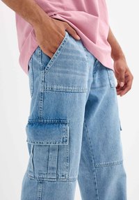 Pantalones cargo de color azul claro con múltiples bolsillos, hechos de tela de mezclilla, con un corte estándar y detalles de costura visibles.
