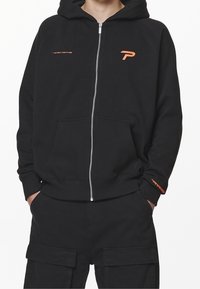 Felpa nera con zip realizzata in misto cotone, dotata di tasca a marsupio, accenti arancioni sul logo e polsini e orlo a coste.