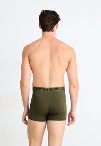 Olivovo zelené boxerky vyrobené z hladkej tkaniny s čiernym elastickým pásom s nápisom "BJÖRN BORG" v veľkých písmenách.
