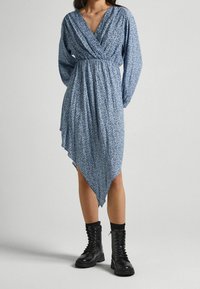 Sininen kukallinen kietaisumekko pitkillä hihoilla, V-päällä ja epäsymmetrisellä helmalla. Yhdistetty mustiin nauhakengiksi. Kevyt, kuviollinen kangas.