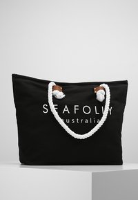 Borsa tote nera in canvas con manici in corda bianca, dettagli in pelle e un logo stampato bianco, caratterizzata da un design spazioso ideale per trasportare oggetti.