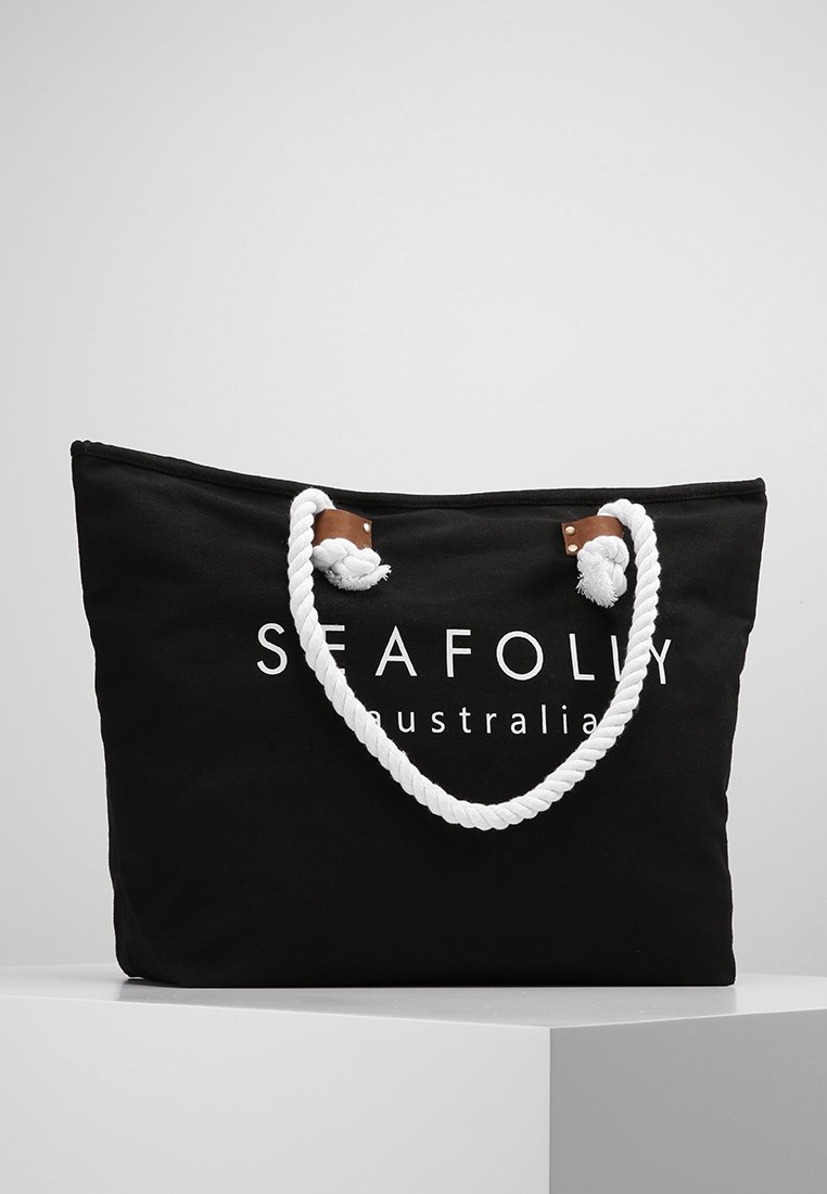 Borsa tote nera in canvas con manici in corda bianca, dettagli in pelle e un logo stampato bianco, caratterizzata da un design spazioso ideale per trasportare oggetti.