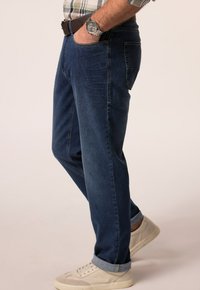 Tmav ě modré džíny v rovné siluetě, s kontrastním prošitím, bočními kapsami a ohrnutými nohavicemi. V kombinaci s lehkými teniskami.