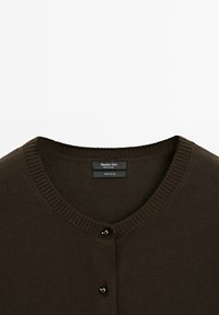 Cardigan in cotone marrone con scollo rotondo, texture a costine e due bottoni neri sul davanti. Etichetta con la scritta "100% cotone, Massimo Dutti."