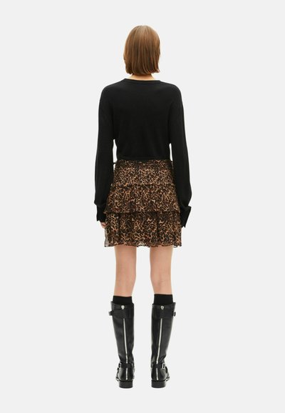Suéter negro, falda de leopardo en capas, botas negras hasta la rodilla con cremalleras y hebillas, y calcetas negras a juego.