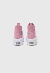 Baskets montantes en toile rose avec semelles blanches, dotées d'un patch logo circulaire et d'une languette arrière pour un enfilage facile.