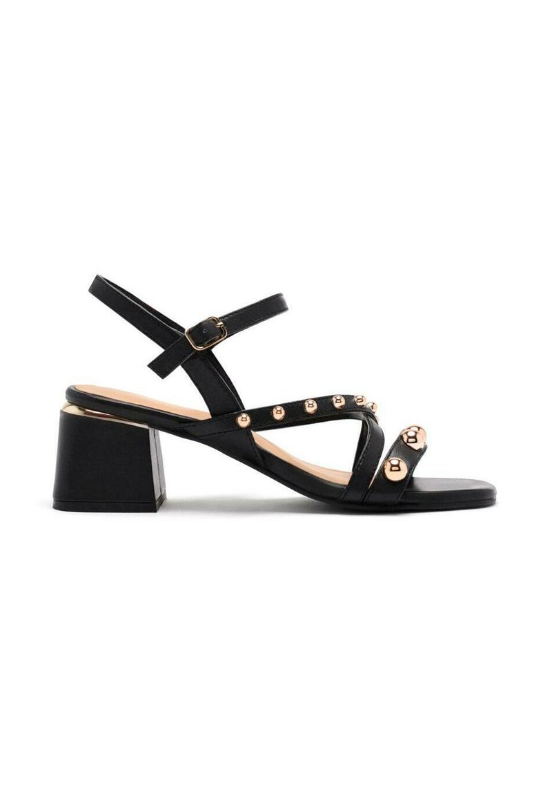 Sandalias de tacón negro con tacón bloque, que cuentan con múltiples correas con detalles en tono dorado y tachuelas redondas, y una textura de cuero suave.