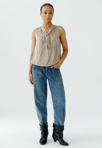 Beige ärmellose Bluse mit einer Schleifendetail, kombiniert mit ausgebleichten blauen baggy Jeans und schwarzen Ankle Boots mit leicht umgeschlagenem Schaft.