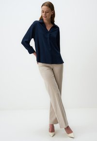 Blusa blu navy a maniche lunghe con scollatura a V e vestibilità rilassata, abbinata a pantaloni beige a gamba dritta e tacchi alti avorio.