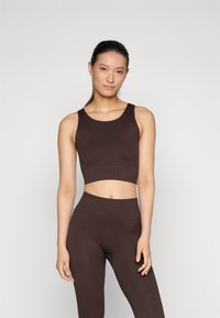Smešani smeđi rebrasti crop top u kombinaciji s usklađenim tajicama visokog struka. Tkanina ima glatku teksturu i kroj koji ističe siluetu.
