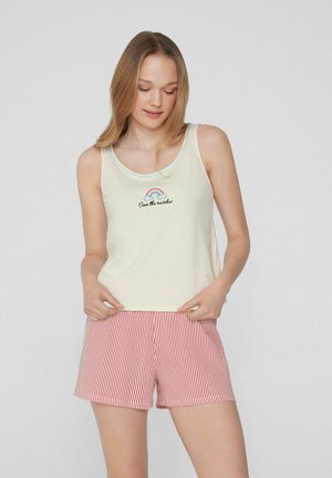 Débardeur crème clair avec un arc-en-ciel et le texte « Au-delà de l'arc-en-ciel » ; associé à un short rayé rouge et blanc. Tissu doux, coupe décontractée.
