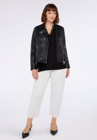 Svart konstläderbikerjacka med gyllene dragkedjor, tillsammans med en svart topp och vita byxor. Jackan har en kortad passform.