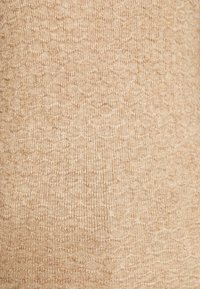 Beżowa dzianina o teksturowanej, lekko wzorzystej powierzchni. Miękka, prążkowana struktura z subtelnymi odcieniami koloru.