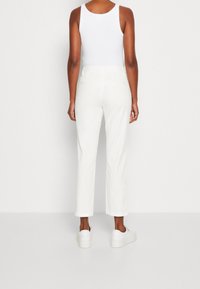 Bílé tapered kalhoty s hladkou texturou, se středním pasem a dvěma zadními kapsami, doplněné bílými slip-on botami.