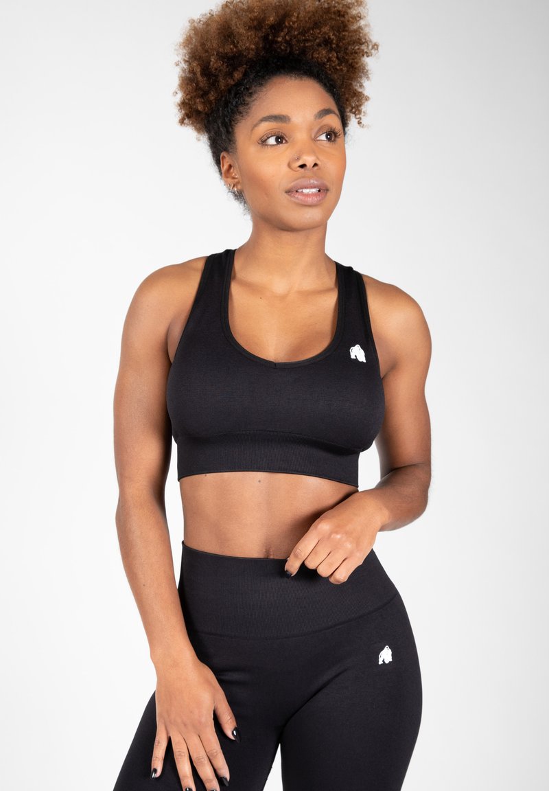 Černý sportovní crop top s kulatým výstřihem, kontrastním logem a ribkovanou strukturou, doplněný o černé legíny s vysokým pasem.