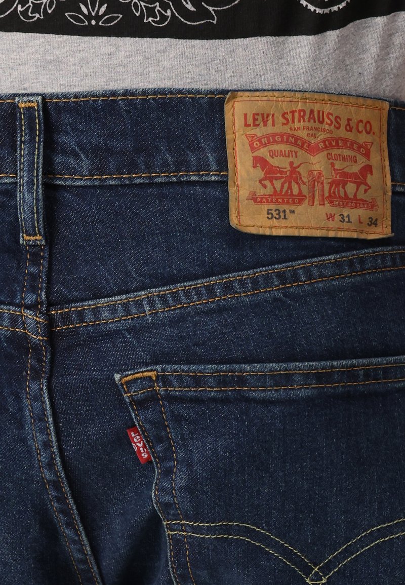 Los jeans de denim azul cuentan con una etiqueta de cuero con "Levi Strauss & Co." y detalles del estilo. Una etiqueta roja enfatizada en el bolsillo trasero izquierdo.