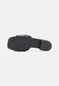 Svart platt sandal med fyrkantig tå och blockklack, som visar texturerad klack och flätad överdel.