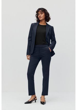 Navy blazer and fitted trousers with a smooth texture, paired with a black top. Footwear is sleek black heels with a pointed toe.