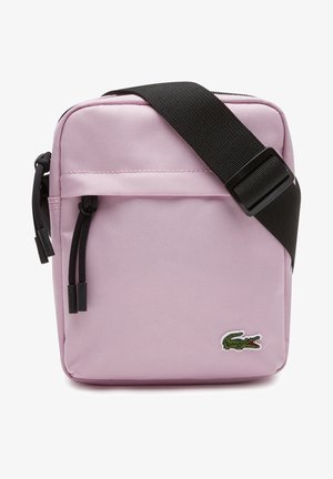 Jasnoróżowa torba na ramię z czarnym regulowanym paskiem, przednią kieszenią na zamek i zielonym logo krokodyla w dolnym prawym rogu.