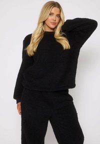 Ensemble de loungewear en polaire noire comprenant un pull texturé et doux avec des épaules tombantes et un pantalon de jogging assorti, tous deux avec des poignets élastiques.