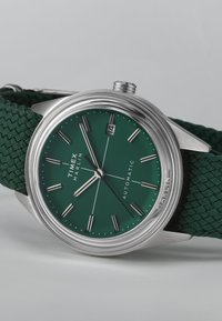 Hodinky Timex Marlin s automatickým strojkom, okrúhlym puzdrom z nehrdzavejúcej ocele, zeleným ciferníkom, striebornými ukazovateľmi hodín, oknom na dátum a textúrovaným zeleným pleteným páskom.
