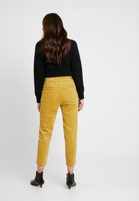 Gula kordtights med smal passform och ankellängd, tillsammans med en svart strukturerad tröja och svarta ankelstövlar.