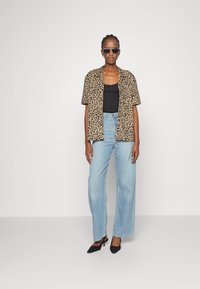 Camisa de manga curta com padrão de leopardo, top preto, jeans de cintura alta azul claro e mules pretos de salto, usados com óculos de sol.