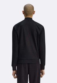 Giacca sportiva nera con collo alto, polsini e orlo a coste, realizzata in tessuto liscio e strutturato con vestibilità morbida.