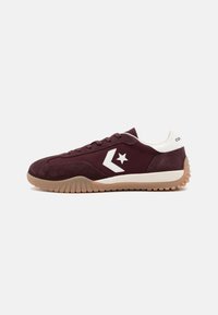 Lågprofil maroon sneaker med vitt stjärnlogotyp, ovandel i mocka och tyg, gummisula och vit vadderad krage på en enkel ljus bakgrund.