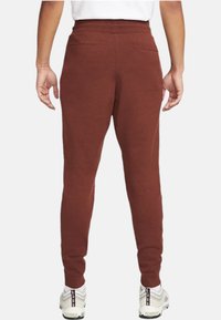 Brown athletic joggers with a tapered design, made of soft fabric, feature back pockets and elastic waistband, paired with white sneakers.