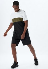 Shorts deportivos negros combinados con una camiseta con bloques de color en blanco, oliva y negro. Presenta una impresión de texto en el pecho.