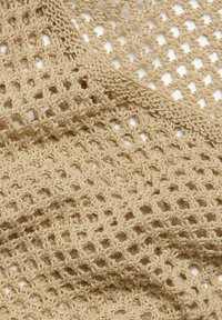 Beige gestrickter Stoff mit einem offenen Webmuster, das eine sichtbare Textur und ineinander greifende Schlaufen aufweist und ein leichtes Aussehen erzeugt.
