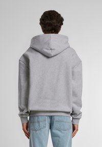 Grå hettegenser med stor åpning bak på halsen og ribbestrikkede mansjetter. Teksturert fleece-materiale, oversized passform, kombinert med lysvaskede denimjeans.