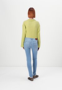 Zelený texturovaný svetr, světle modré skinny džíny a baleríny s leopardím vzorem. Oblékání je neformální, s viditelnými kapsami a detaily límečku.