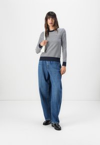 Stripet langermet genser i marineblå og hvit, sammen med løse blå jeans. Antrekket har ribbestrikkede mansjetter og en minimalistisk hvit veske.