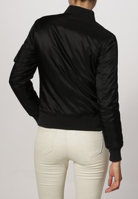 Giacca bomber nera in satin con vita e polsini aderenti, caratterizzata da un design semplice e con minimalismi sul retro.