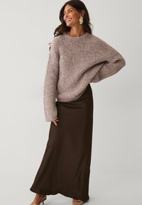 Lysbrun strikket sweater med overdimensionerede ærmer, parret med en lang, mørkebrun satin-nederdel. Brune hæle.