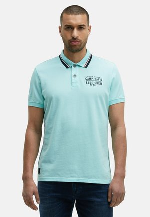 Helles blaues Polohemd mit kontrastierendem dunklem Kragen, das ein kleines Logo und Text auf der Vorderseite trägt. Hergestellt aus strukturiertem Stoff, im taillierten Stil.