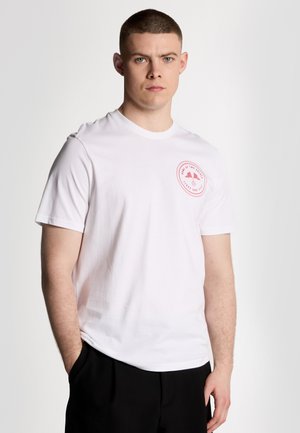 T-shirt en coton blanc à manches courtes, avec un col rond et un logo rouge circulaire imprimé sur la poitrine gauche.