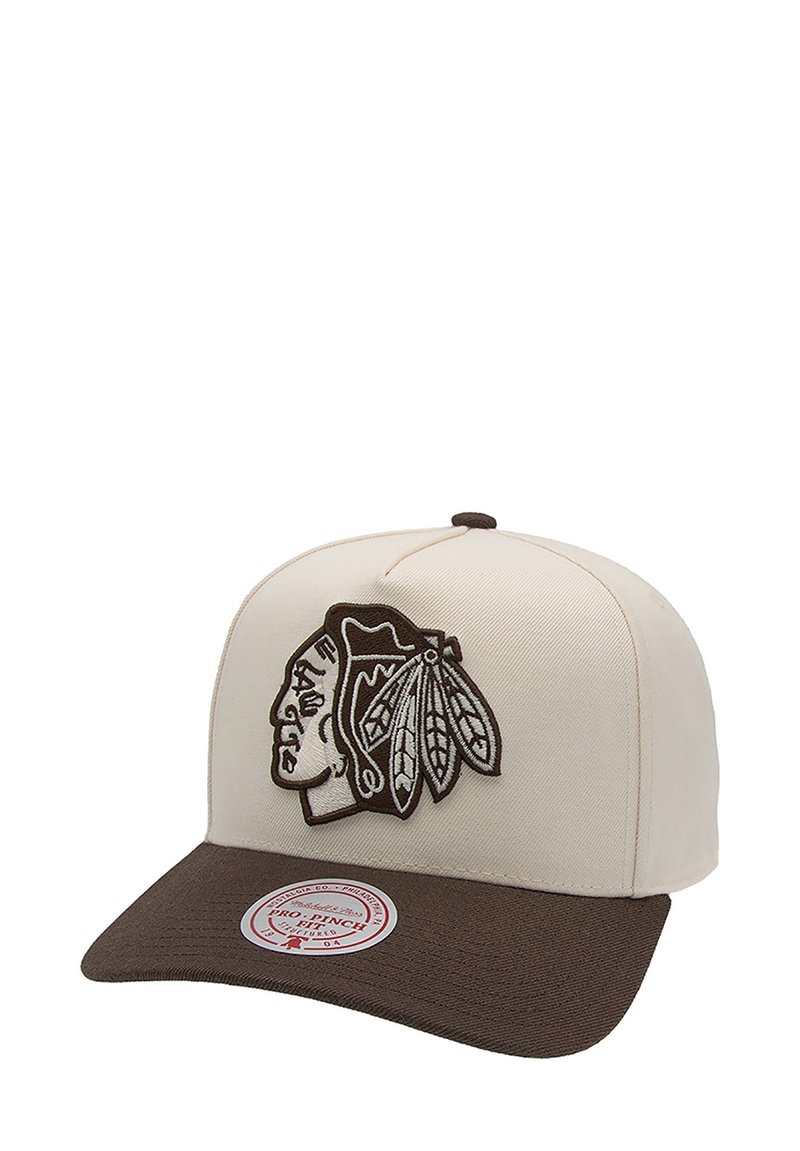 Casquette de baseball avec un dessus en toile crème, un visière brune et un logo brodé de tête amérindienne avec des plumes. Comprend un détail d'autocollant.