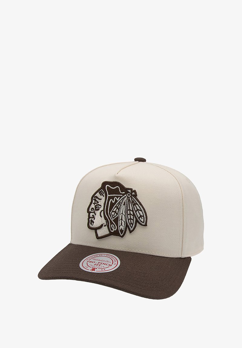 Baseballmütze mit einer cremefarbenen Canvas-Oberseite, brachem Schirm und gesticktem Logo eines indianischen Kopfes mit Federn. Inklusive Aufkleberdetails.