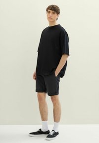 Czarna, oversize krótka koszulka z krótkim rękawem w połączeniu z ciemnymi szortami, białymi skarpetkami i czarnymi trampkami. Prosty design o luźnym kroju.