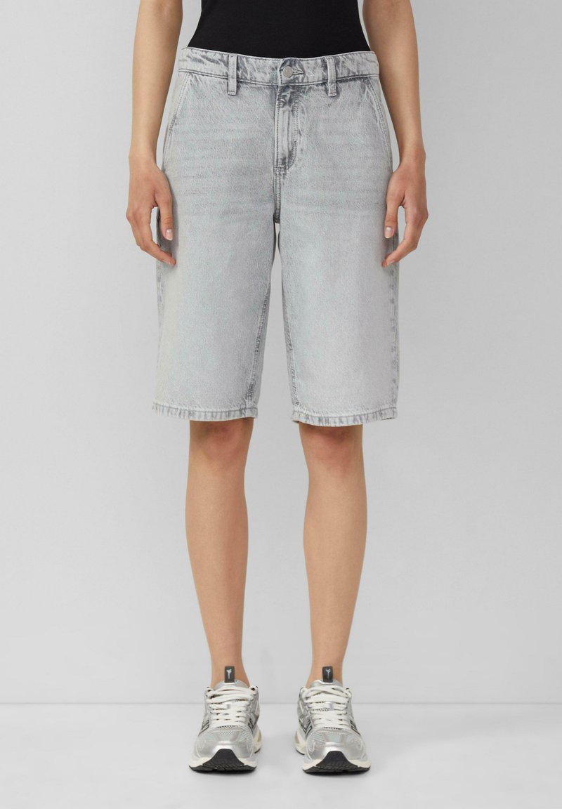 Shorts en denim gris clair avec une taille haute, une jambe droite et des bords ourlés. Portés avec des baskets argentées et un haut noir.