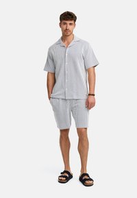 Conjunto de camisa de algodón de manga corta a rayas en azul y blanco, y pantalones cortos a juego, con cierre de botones y corte holgado. Sandalias completan el look.