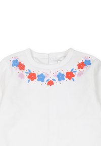 Witte katoenen kleding met een kleurrijke bloemembroiderie in rood, blauw en roze rond de halslijn, met een knoopsluiting aan de achterkant.