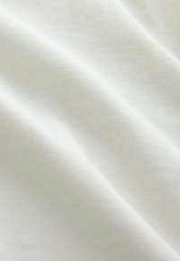 Nærbillede af blød, glat hvidt stof med subtil tekstur og bløde folder, der skaber lys- og skyggevariationer.