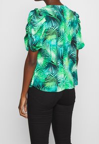 Blusa a maniche corte con stampa a foglie in diverse tonalità di verde. Presenta maniche arricciate e chiusura con bottone sul retro.