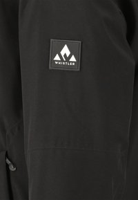 Zwarte waterdichte jas met een gladde textuur. Kenmerkt zich door een merkpatch met een berglogo en het woord "WHISTLER."